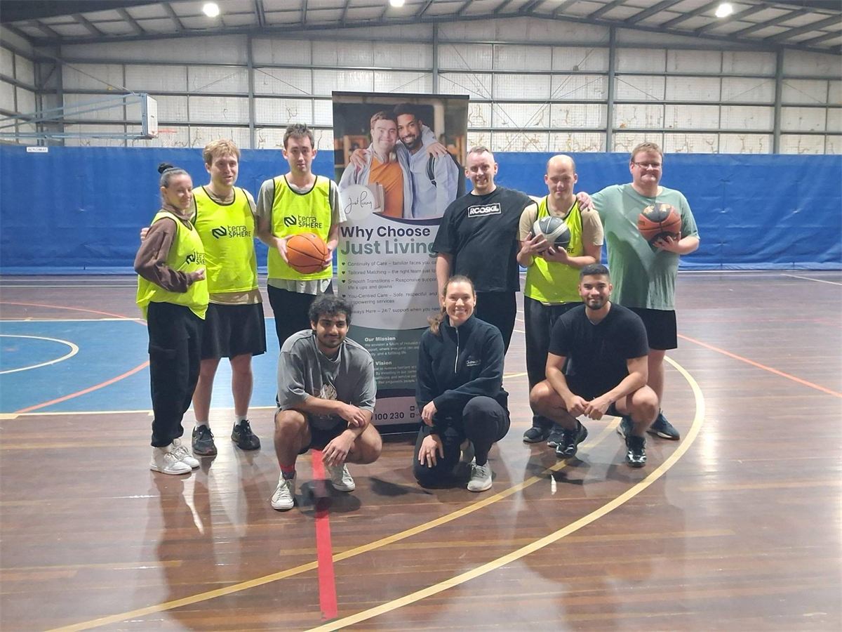 Inclusive Basketball players and volunteers together on the court beside a Just Living banner