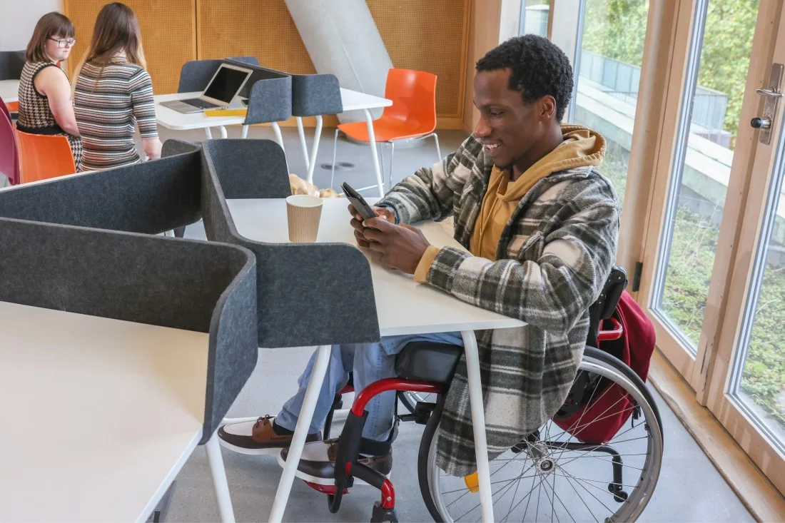 A man using a wheelchair smiles as he reads a message on his phone